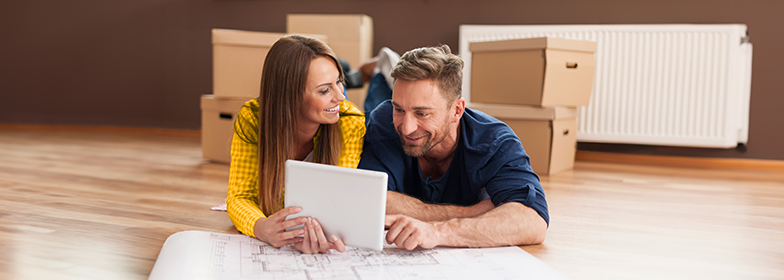 Smiling couple laying on ground with blueprints